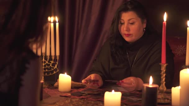 Wahrsagerin Frau im dunklen Raum mit vielen Kerzen rät auf einem Tarot-Kartenspiel — Stockvideo