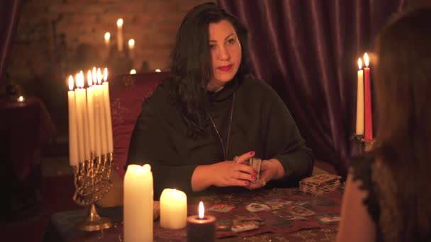 카드 레이아웃을 사용하여 타로 카드 갑판에 촛불 추측의 많은 어두운 방에서 점쟁이 여자 — 비디오
