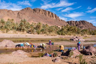 Ourzazate, Fas - Ocak 2019: Berberi kadınlar güzel pitoresk yerde Vaha de Fint nehirde çamaşır yıkayın. Su günü yoksul Fas kabileleri