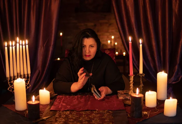 Cajero de la fortuna mujer en habitación oscura con un montón de adivinanzas velas en una baraja de cartas del tarot — Foto de Stock