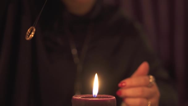 Fortune teller vrouw in donkere kamer met veel kaarsen geeft een uitleg van de toekomst en voorspelling van het lot aan een klant met behulp van gouden trouwring — Stockvideo