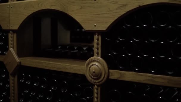 Vinflaskor ligger i stapeln i källaren. Glasflaskor rött vin lagrat i trä hyllor i stenkällare. Interiör underjordisk vinkällare i vingård — Stockvideo