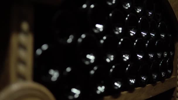 Close up shot of Wine bottles lying in stack at cellar. Glass bottles of red wine stored in wooden shelving in stone cellar. Interior underground wine cellar in winery — Stock Video