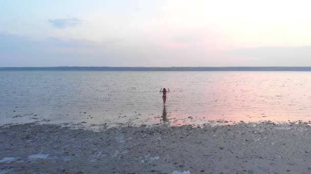 Egy lány sziluettje a tó közepén naplementekor. Gyönyörű lány pózol egyedül sekély vízben fényhullámokkal — Stock videók