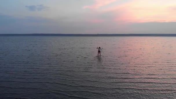 Silhuett av en flicka mitt i sjön vid solnedgången. Vacker flicka poserar ensam i grunt vatten med lätta ringar — Stockvideo