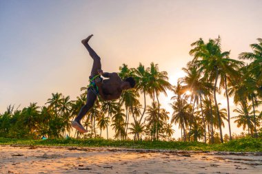 Beyaz Kum Sahili Akrobasi Eğitiminde Genç Çekici Kaslı ve Güçlü Siyah Afrikalı Adam ve Gün batımında Atlayan Jimnastik Sahili Gösterisi