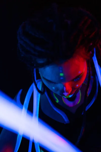 Retrato de uma garota de guerra com tubos brilhantes em Neon UF Light. Menina modelo com Dreadlocks e maquiagem psicodélica criativa fluorescente, Design de arte do modelo de dançarina de disco feminino em UV, abstrato colorido — Fotografia de Stock