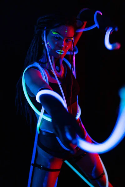 Retrato de uma garota de guerra com tubos brilhantes em Neon UF Light. Menina modelo com Dreadlocks e maquiagem psicodélica criativa fluorescente, Design de arte do modelo de dançarina de disco feminino em UV, abstrato colorido — Fotografia de Stock