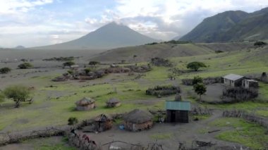 Günbatımında Afrika 'nın kuzey Tanzanya bölgesindeki Arusha Bölgesi' nde Engare Sero köyü Maasai dilinde Tanrı 'nın Dağı Ol Doinyo Lengai' nin önündeki Maasai köyü üzerinde Uçan Sinek Manzarası.