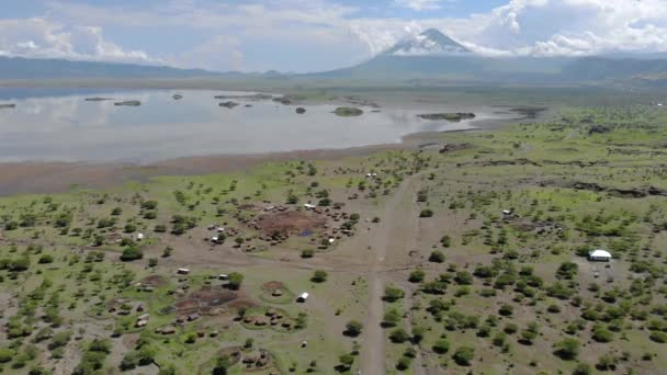 Flyby lotnicze Widok na wioskę Maasai na wybrzeżu jeziora Natron przed Ol Doinyo Lengai, Góra Boga w języku maasai, Engare Sero wsi w regionie Arusha i północnej — Wideo stockowe