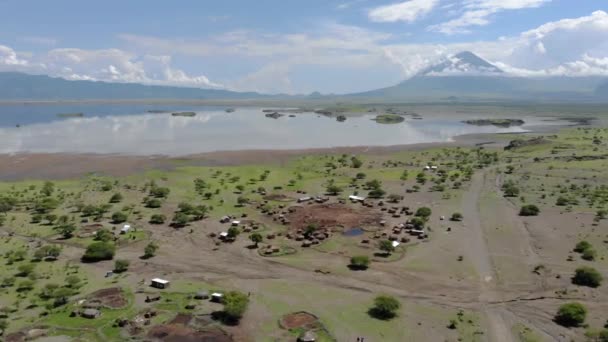 Flyby lotnicze Widok na wioskę Maasai na wybrzeżu jeziora Natron przed Ol Doinyo Lengai, Góra Boga w języku maasai, Engare Sero wsi w regionie Arusha i północnej — Wideo stockowe