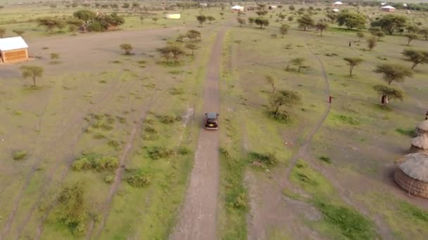 Πυροβολισμός από εναέριο drone. Μαύρο αυτοκίνητο κινείται μέσα από το παραδοσιακό χωριό Masai στο Sunset time κοντά στο Mto wa Mbu, Αρούσα, Τανζανία. — Αρχείο Βίντεο