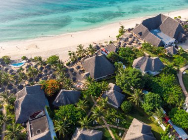 Havuz manzarası, şemsiyeler, yeşil palmiye ağaçları olan kumlu plaj. Yazın günbatımında Hint Okyanusu kıyısında. Zanzibar, Afrika. Üst Manzara. Gök mavisi suları, şemsiyeleri, palmiyeleri olan bir manzara. Lüks.