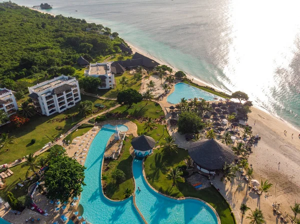 Vista aérea de piscina, sombrillas, playa de arena con palmeras verdes. Costa del océano Índico al atardecer en verano. Zanzíbar, África. Vista superior. Paisaje con agua azul, sombrillas, palmeras. Lujo — Foto de Stock