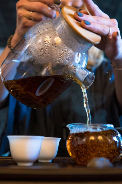 伝統的な中国茶の儀式。紅茶や紅茶をグラスティーポットからグラスチャイに注ぐ暗い木製のテーブルの背景 — ストック写真