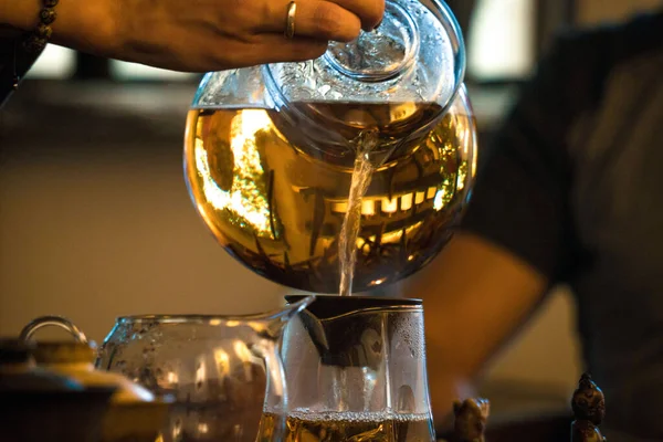 伝統的な中国茶の儀式。紅茶や紅茶をグラスティーポットからグラスチャイに注ぐ暗い木製のテーブルの背景 — ストック写真
