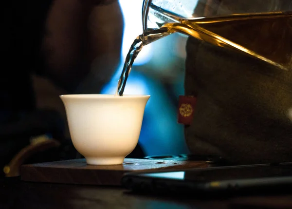 Ceremonia tradicional del té chino. Té negro o rojo que se vierte desde un cristal ver a través de Chahai en la taza pial blanca sobre fondo de mesa de madera oscura —  Fotos de Stock