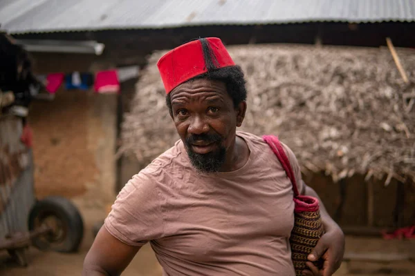 Retrato de um homem mais velho africano em vermelho muçulmano Taqiyyah Fez Chapéu posando com uma vara para pessoas coxos no quintal Perto da cabana básica com telhado coberto em pequena aldeia remota na Tanzânia, ilha de Pemba — Fotografia de Stock