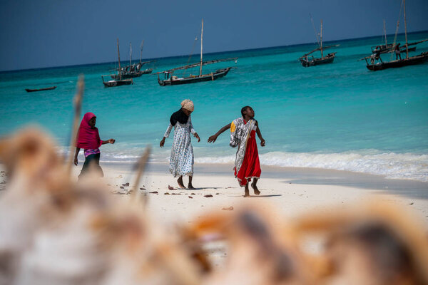 ZANZIBAR, TANZANIA - JANUARY 2020: Three Young local girls on the beach with Turquoise Water and Dhow Boats in Ocean in Nungwi, Zanzibar