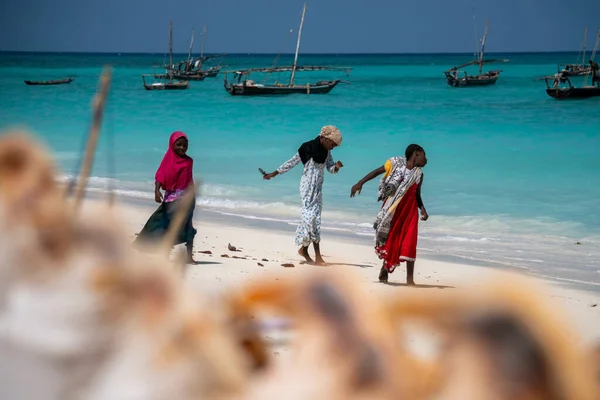 ZANZIBAR, TANZÂNIA - JANEIRO 2020: Três jovens garotas locais na praia com água azul-turquesa e barcos Dhow no oceano em Nungwi, Zanzibar — Fotografia de Stock