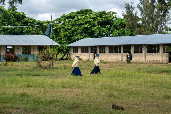 Isla de Pemba, Zanzíbar, Tanzania - Enero 2020: Dos niñas de primaria llevan su libro en la cabeza y se mueven por el patio escolar en uniforme — Foto de Stock