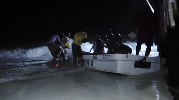 NUNGWI, ZANZIBAR - JAN 2020: Zanzibarの熱帯夜の嵐。黒いアフリカの人々のグループは、嵐の海からモーターボートを救うバケツで水をすくい取る — ストック動画