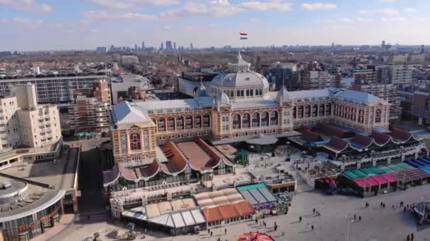 Tha Hague, Paesi Bassi - Marzo 2020: Veduta aerea degli uccelli su una bandiera sulla cima del Kurhaus di Scheveningen Situato sulla costa olandese. Lunga spiaggia di sabbia un lungomare e un molo al Mare del Nord popolare — Video Stock