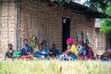 Afrikalı siyahi kadın ve çocuklar Tanzanya 'da sazdan yapılmış sopa ve çamurdan yapılmış kır evinin yanında oturuyorlar. Doğudaki Swahili halkının gelişmekte olan ulus ve kültürünün yoksulluğu