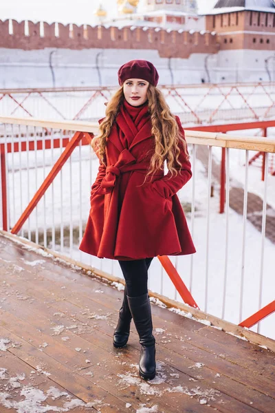 Ένα όμορφο κορίτσι με ένα κόκκινο παλτό και ένα μπερέ περπατάει κατά μήκος του — Φωτογραφία Αρχείου