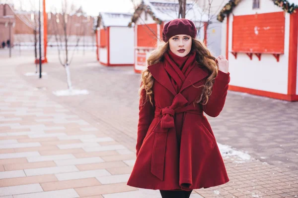 A beautiful girl in a red coat and a beret is walking along the — Stock Photo, Image