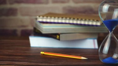Ağır çekim dolly kalem ve kitap ile kum saati ahşap masanın üstüne yığılmış. Kavramları öğrenme ve eğitim.