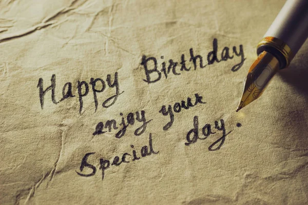 Vintage brass pen writing birthday greetings on old paper.