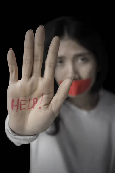 Abused woman showing help word on her palm with her mouth covered by red tape