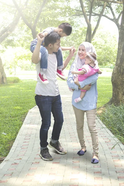 在公园散步时抱着孩子的快乐父母的全长 — 图库照片