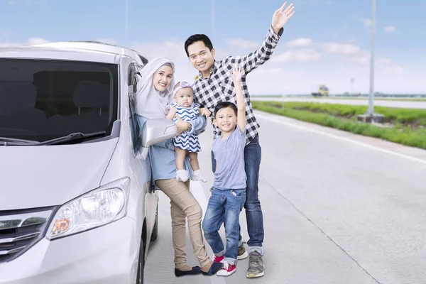 Portrait of Muslim family waving hands together at the camera while standing on the road near their car