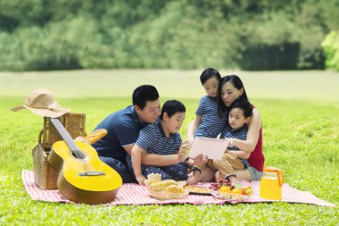 Parkta piknik sırasında dijital tablet ile oynayan Çinli aile fotoğrafı