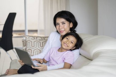 Genç Anne ile kızı birlikte kanepede bir dizüstü bilgisayar kullanırken kameraya gülümseyen