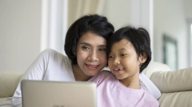 Genç kadın kanepede otururken bir dizüstü bilgisayar kullanarak kızı öğretim. Evde vurdu