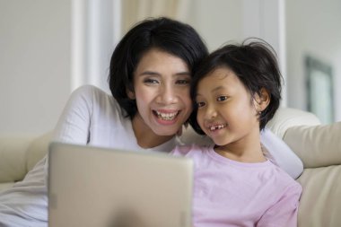 Kızıyla birlikte kanepede otururken bir dizüstü bilgisayar kullanarak bir genç kadın resim 