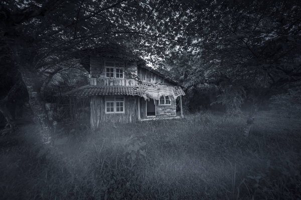 Image of abandoned wood house looks haunted with damaged rooftop. Shot at night time