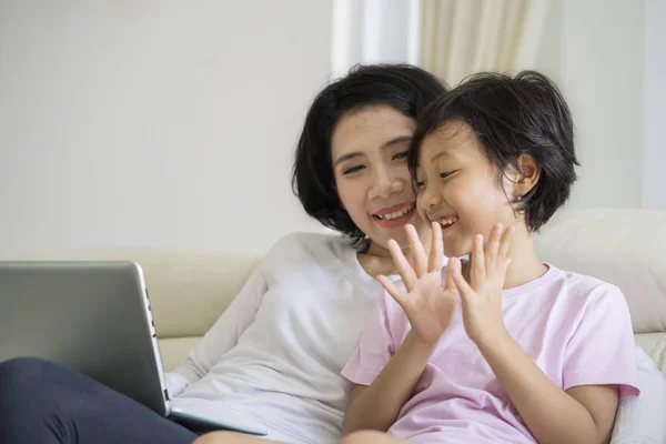 小女孩的图片使用膝上型电脑与她的母亲 而坐在沙发上愉快的表情 — 图库照片