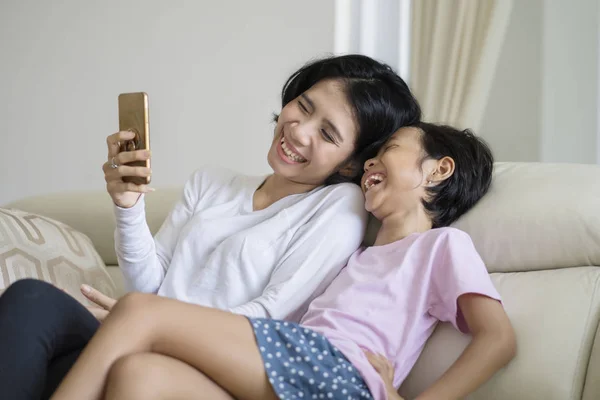 Mujer Joven Usando Teléfono Móvil Mientras Ríe Con Hija Sofá — Foto de Stock