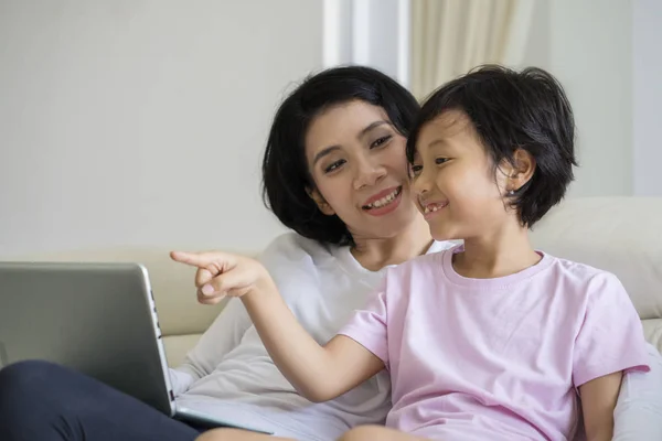 亚洲妇女图片引导她的女儿坐在沙发上使用笔记本电脑 — 图库照片