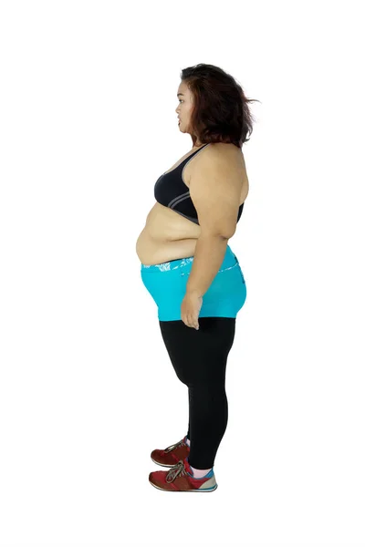 スポーツウェアを着て 白い背景に分離されたスタジオに立ってながら物思いに見える肥満女性の側面図 — ストック写真