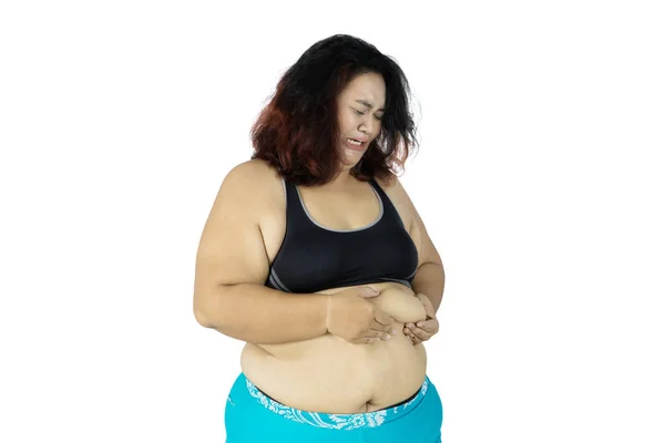 悲伤的肥胖妇女穿着运动服 而捏她的腹部脂肪 孤立的白色背景 — 图库照片