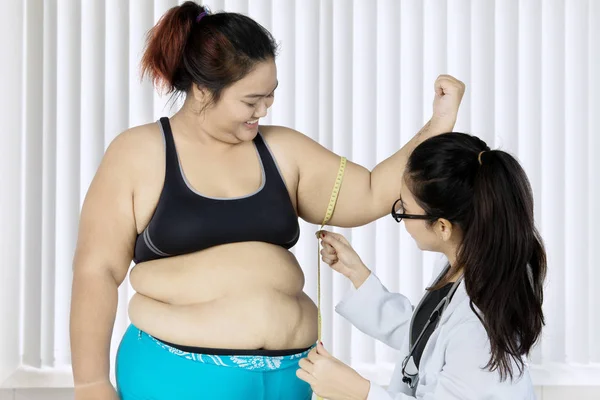 年轻女医生在诊所检查时用卷尺测量她肥胖病人的二头肌 — 图库照片