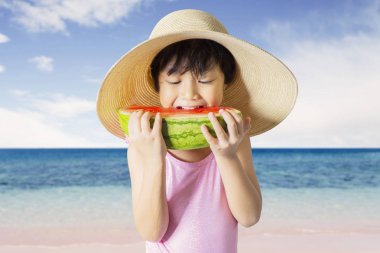 Yaz konsepti. Sevimli küçük kız sahilde bir dilim karpuz dururken yeme