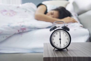 Çalar saat tablo ve genç kadını yatağa sleeped resmi. Evde vurdu