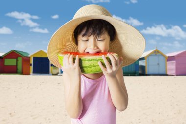 Sahilde bir dilim karpuz dururken yeme bir küçük kızın resmi. Yaz kavramı