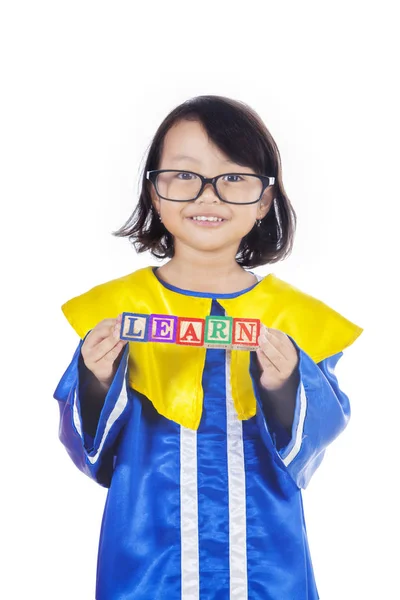 可爱的小女孩穿着毕业礼服 而持有学习字在木立方体上 孤立的白色背景 — 图库照片